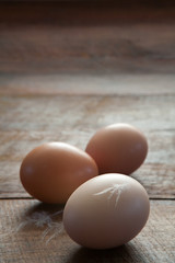 Vertical Close Up of Three Fresh Farm Chicken Eggs and Feathers on a Dark Brown Rustic Wooden Farm Table with Copy Space