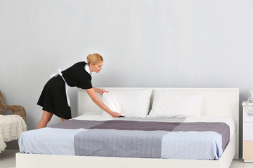 Chambermaid making bed in hotel room