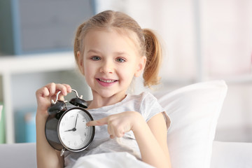 Cute little girl with alarm clock in bed