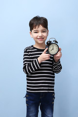 Fototapeta premium Cute little boy with alarm clock on color background