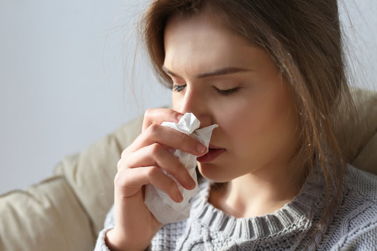 Young ill woman with tissue sitting on lounge at home