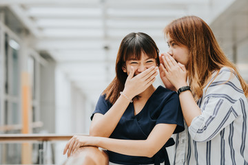 Young Asian girl whispering gossip or secret to her friend with smile and laugh