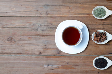 A cup of hot tea and spices on a wooden table.