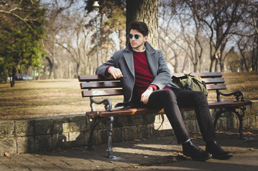 Young male hipster sitting in park on winter sunny day