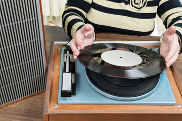 Old woman sitting at a table puts vinyl record on retro player, close-up