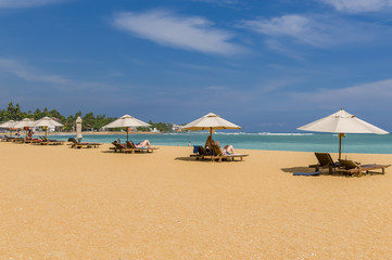 Tropischer Strand mit Holzliegen und Sonnenschirme mit weißem Sand und türkis blauem Meer