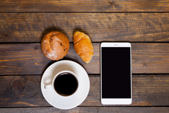 Mobile phone with white mug of coffee and croissants