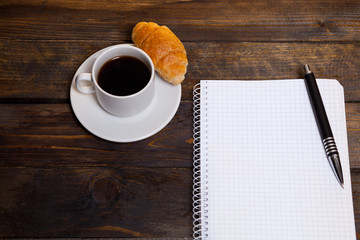 View from above. Mobile phone with white cup of coffee and notepad on wooden background. Workspace flat lay.