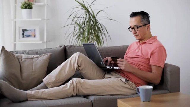 man with laptop and credit card on sofa at home