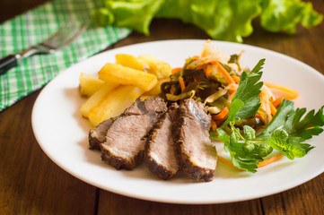 Roast beef sliced slices with fries and greens. Wooden background. Close-up