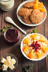 A light breakfast of cereal, jam, milk, biscuits and fruit. Wooden background. Top view. Close-up