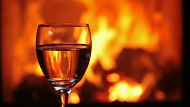 Wine glass in front of fireplace slowly coming into focus - woman hand taking it, closeup, rack focus