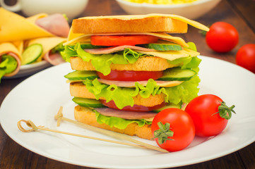 Big sandwich, meat, lettuce, cheese and vegetables on toasted. Wooden background. Close-up