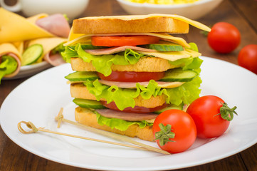 Big sandwich, meat, lettuce, cheese and vegetables on toasted. Wooden background. Close-up