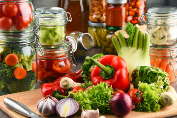 Jars with marinated food and raw vegetables on cutting board