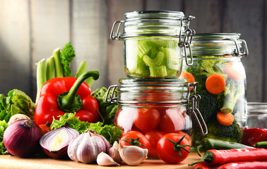 Jars with marinated food and raw vegetables on cutting board