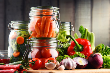 Jars with marinated food and raw vegetables on cutting board