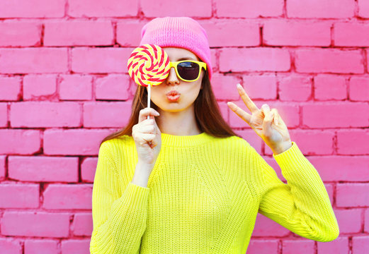 Fashion portrait pretty cool girl with lollipop having fun over colorful pink brick background