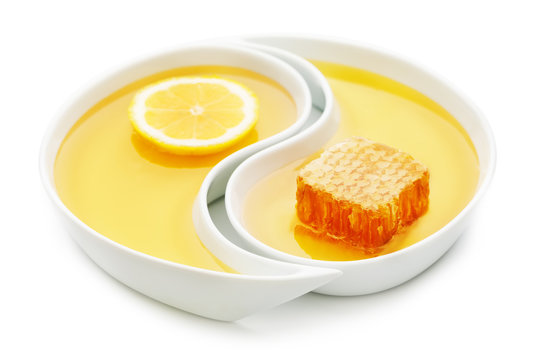 Honey, a honeycomb and a slice of lemon in two yin yang trays, isolated on white