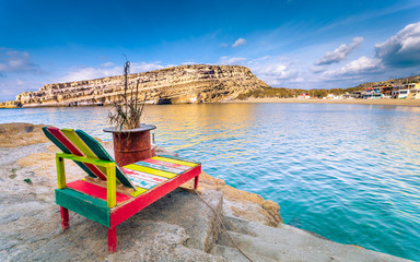 Matala beach with a colorful wooden long chair and the caves on the rocks that were used as a roman cemetery and at the decade of 70's were living hippies from all over the world, Crete, Greece