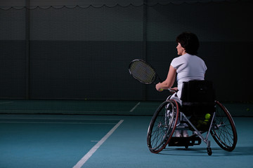 Disabled mature woman on wheelchair playing tennis on tennis court.