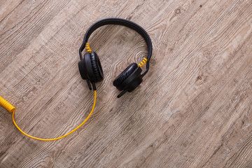 Headphones with yellow cable. Modern device for listening music. Sound earphones lying on wooden rustic background.