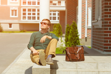 Young man enjoy to the music with a tablet with headphones, while sitting outdoors. Guy sat down to rest and listen to the audiobook.