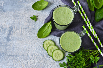 Obraz na płótnie Canvas Green vegetable smoothie with avocado, cucumber and spinach on a gray background. Top view.