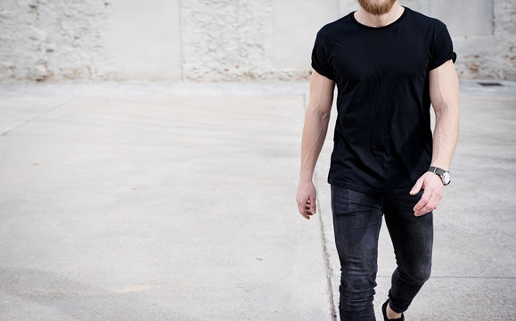 Young muscular man wearing black tshirt and jeans walking on the urban district. Blurred background. Hotizontal mockup.
