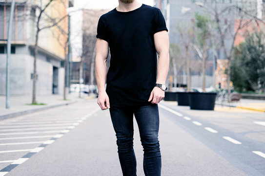 Young muscular man wearing black tshirt and jeans posing on the street of the modern city. Blurred background. Hotizontal mockup.