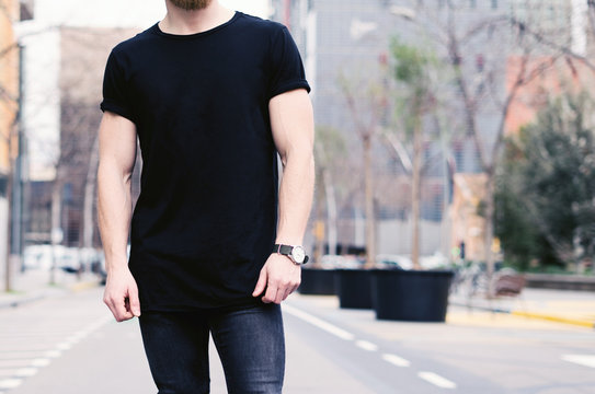 Closeup view of young muscular man wearing black tshirt and jeans posing on the street of the modern city. Blurred background. Hotizontal mockup.