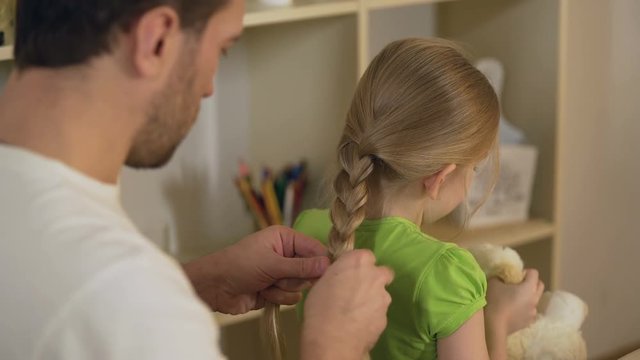 Responsible good father braiding little daughter's hair, preparations for school