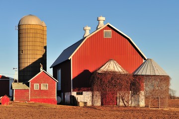 On a bright winter day, a red barn, silos and empty storage cribs await spring in front of a farm...