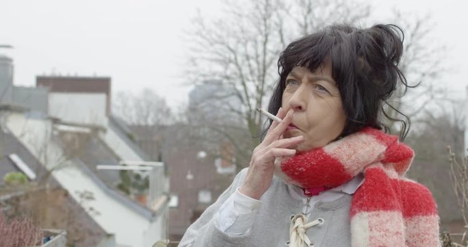 modern elderly french woman with red & white scarf smoking a cigarette in winter on a rooftop terrace (BEST AGER WOMAN) 