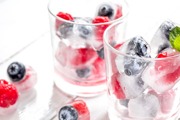 Icecubes with blueberry and raspberry in glass on wooden table