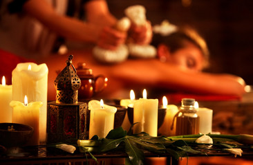 Massage of woman in spa salon. Girl in massaging spa salon. Luxary interior in oriental therapy salon. Close up of female massage hands give herbs hot ball therapy. Burning candles on foreground.