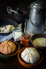 home made cheese over a rustic wooden table with its ingredients, milk, salt, paprika, curd and an old milk churn