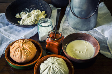 home made cheese over a rustic wooden table with its ingredients, milk, salt, paprika, curd and an old milk churn