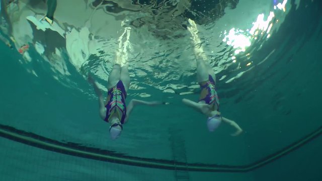 Synchronized swimming, two girls training, underwater view.
