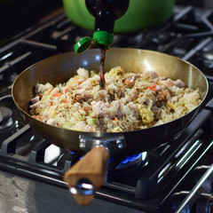 adding soy sauce to fried rice in wok over gas flame stove