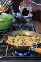 man sprinkles salt on fried rice in wok over gas flame stove