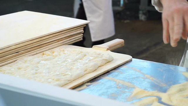 Baker stretching dough of a focaccia on a wooden cutting board