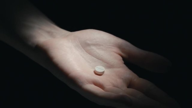 male pours bunch of pills into the palm of her hand in a dark room.
