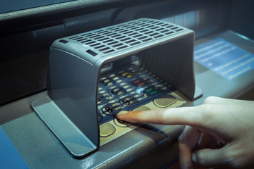 finger point at A.T.M. numpad keypad with guard for protect and use deposit or withdraw money, closeup