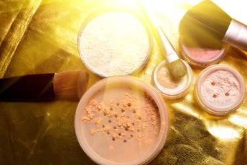 Set of decorative cosmetics on a golden shiny background. Powder, shimmer, eye shadow, blush and brushes on wooden background, beauty and makeup concept with sunlight