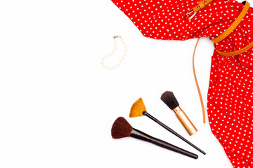 flat lay feminine red dress, pearl bracelet and makeup brushes on white background.