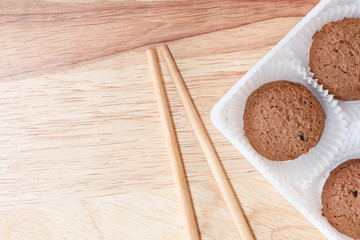Cookies chocolate in plastic box and chopsticks on wood background