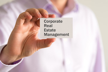 Businessman holding a card with text Corporate Real Estate Management