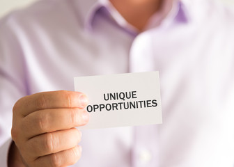 Businessman holding a card with text UNIQUE OPPORTUNITIES