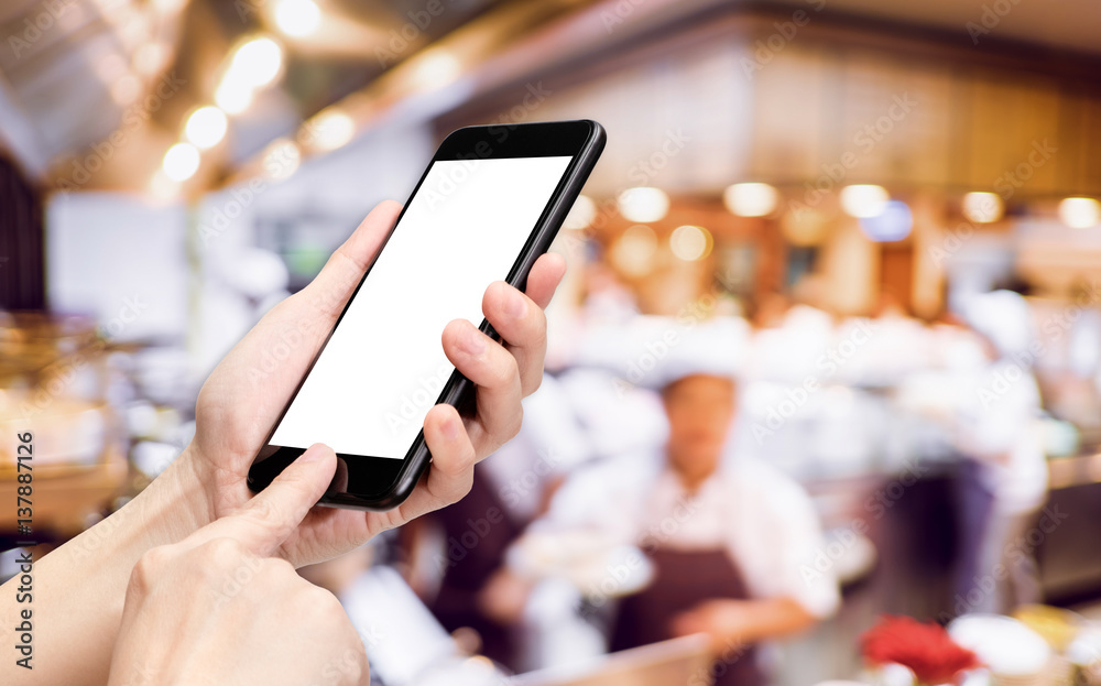 Leinwandbilder Hand click mobile phone with blur chef at restaurant background bokeh light,White screen mock up template for adding your design or your text
